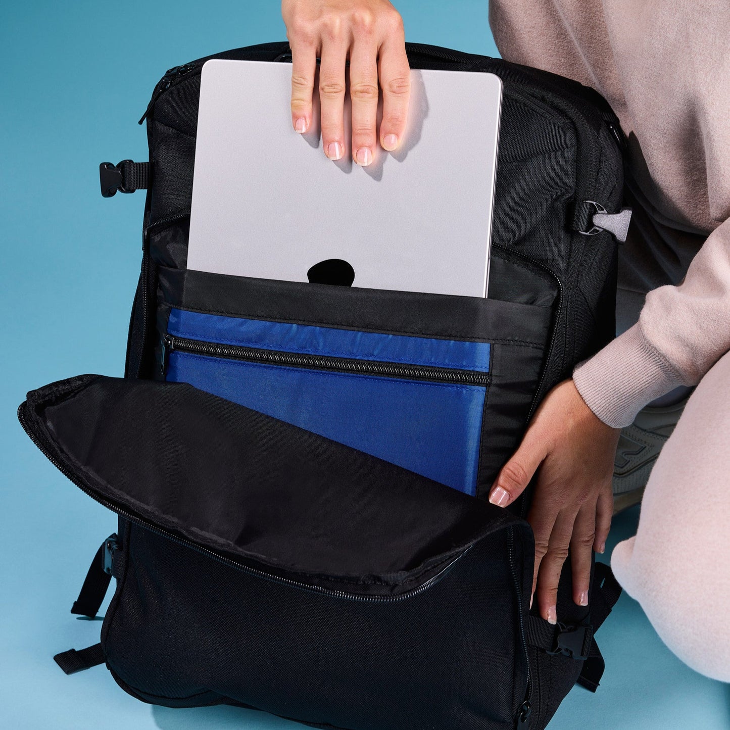 Traveler placing a laptop into the Swae Flow 40L Travel Backpack’s secure, padded 16" laptop pocket, designed for digital nomads and business travellers.