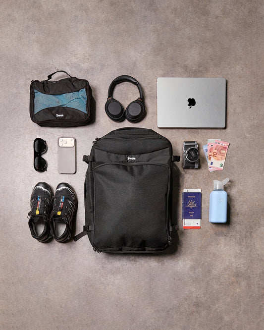 Swae Flow 40L travel backpack flat lay with packing cube, laptop, headphones, passport and travel essentials for carry-on travel.