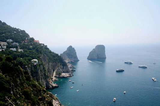 Scenic view of Capri, Italy with cliffs, Faraglioni rocks, and yachts on blue sea, overlaid with text: Capri, Italy: Carry-On Travel Guide.
