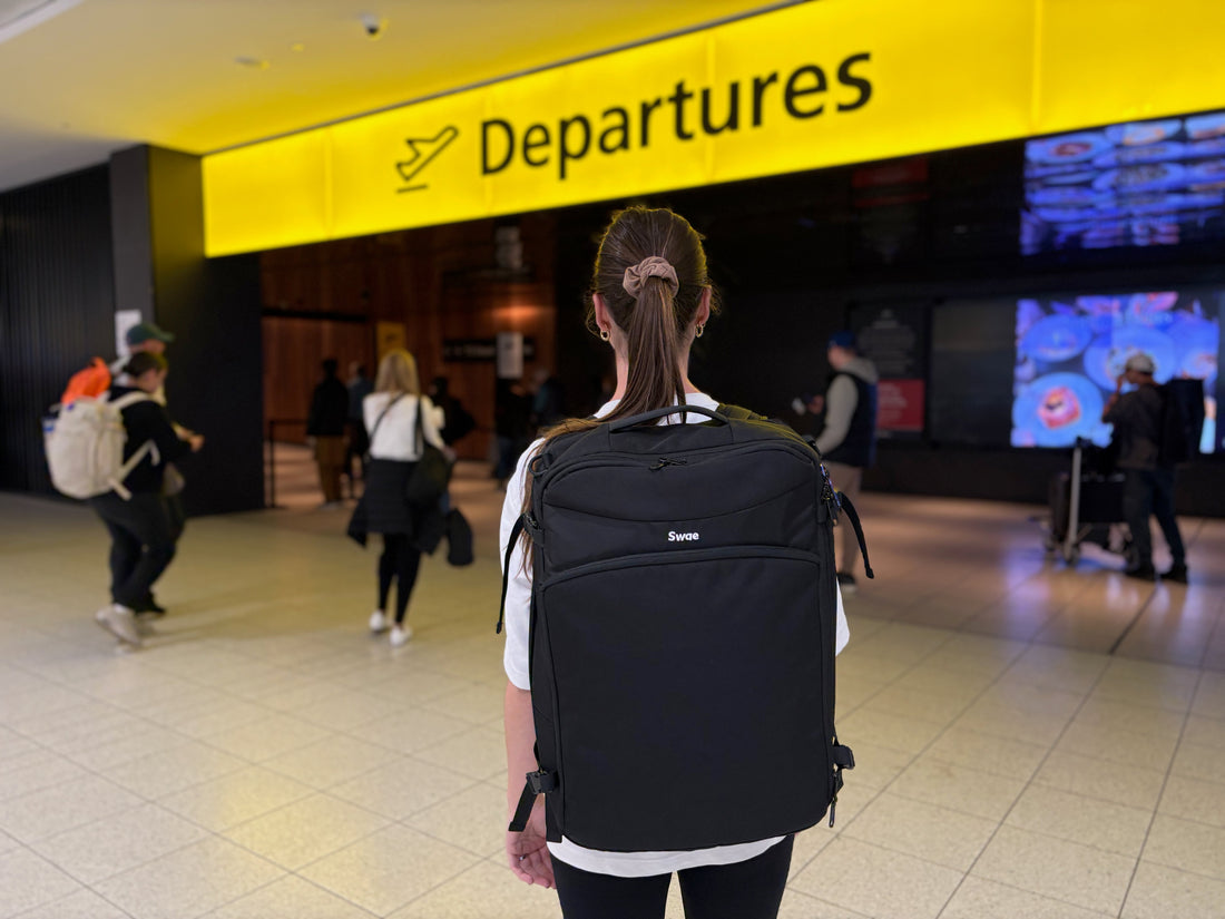 Traveller wearing a Swae backpack standing in front of an airport departures entrance.