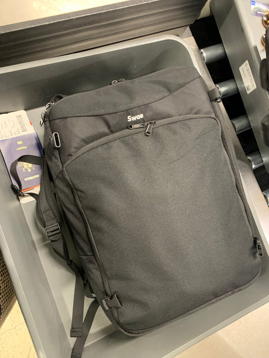 Swae Flow 40L carry-on backpack in airport security tray with passport and boarding pass, showing its fit for carry-on air travel.