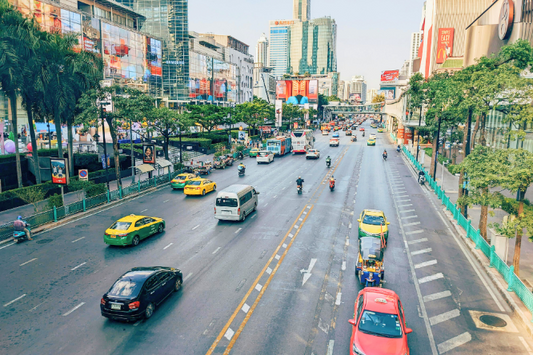 Bangkok city street with colorful taxis, motorbikes, shopping malls, and tall buildings.