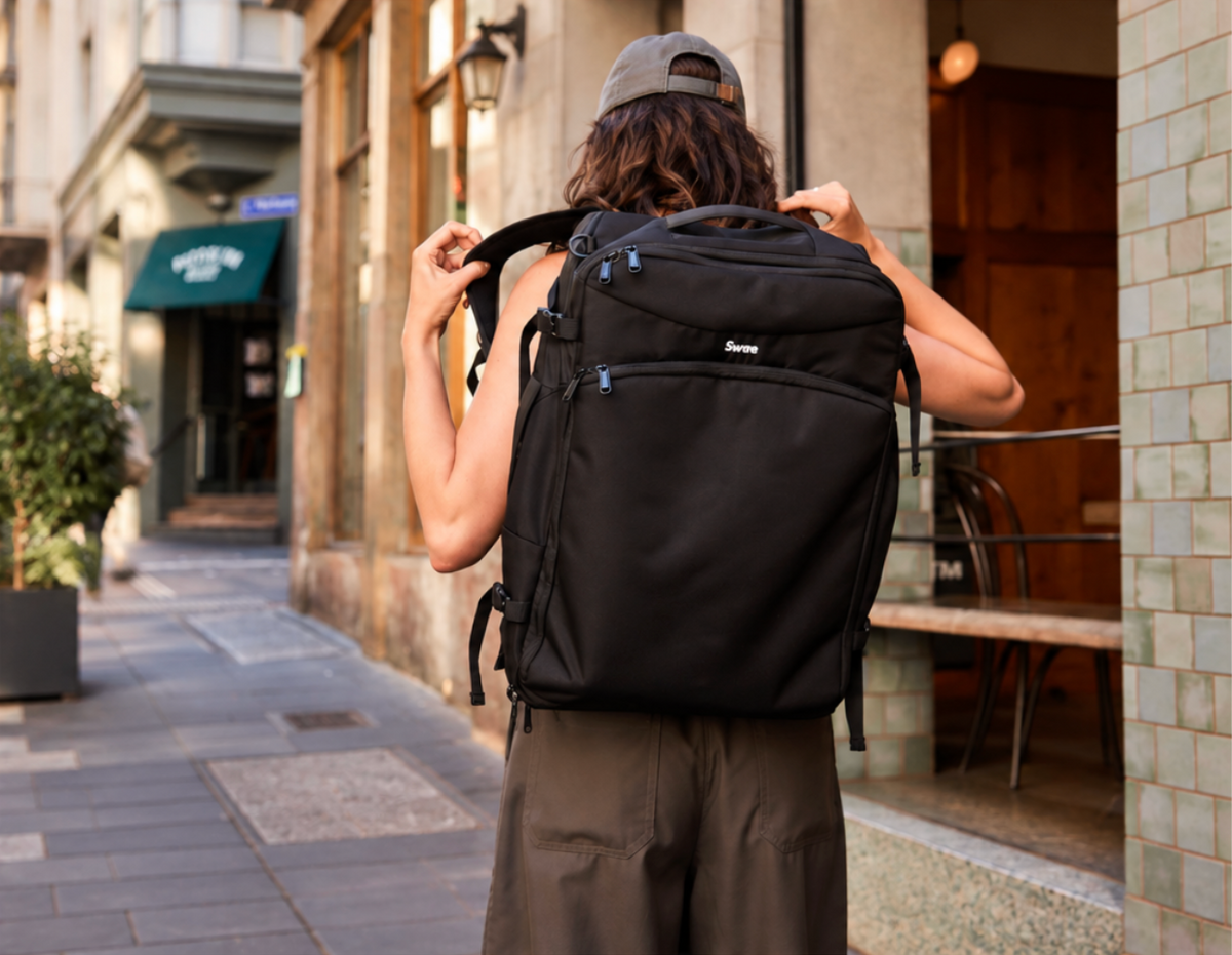 Traveller wearing a black Swae 40L carry-on backpack while walking through a city street.